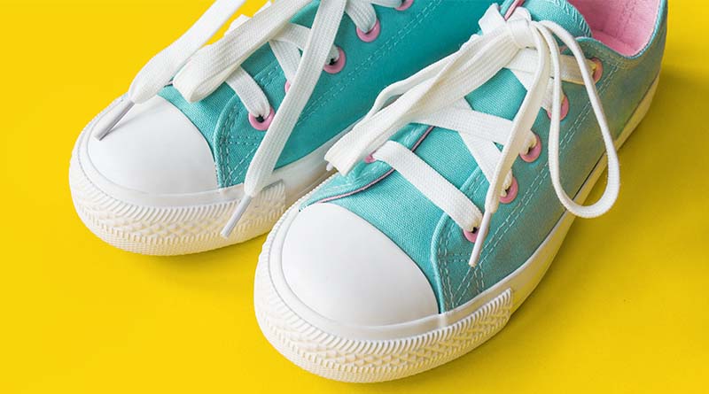 A pair of teal and white wide fit shoes with laces on a yellow background